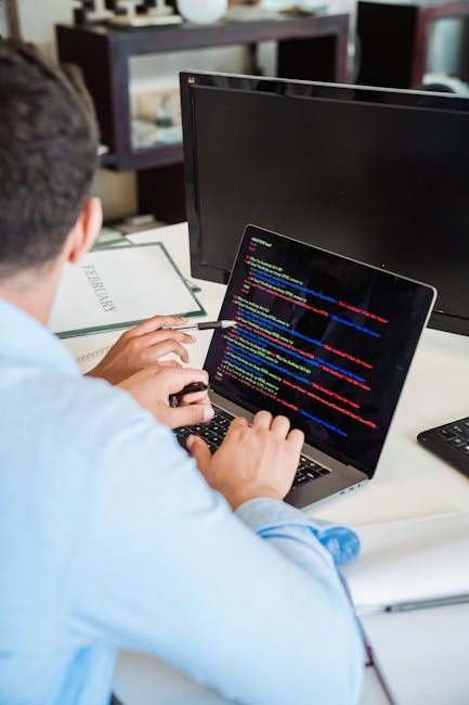 A close-up photograph of a computer screen displaying lines of HTML code in various colors, including orange, blue, yellow, and green, with tags such as <h1>, <div>, <img>, and <section>. The code app